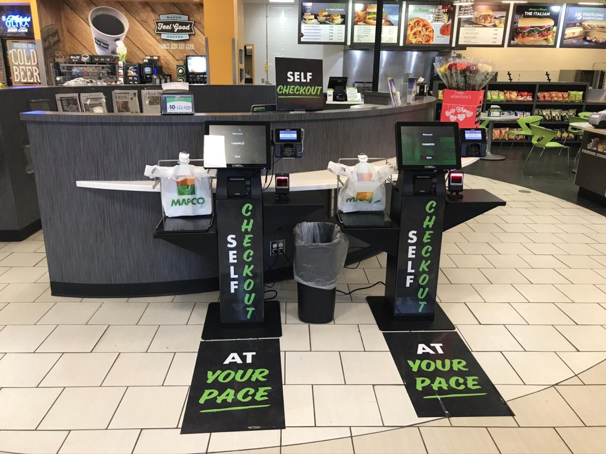 Two self-checkout lanes at a c-store advertising shopping 